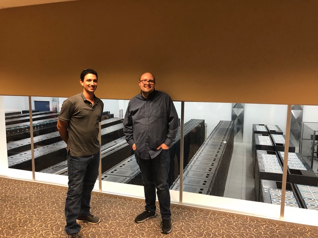 Two men standing outside a room full of server cabinets