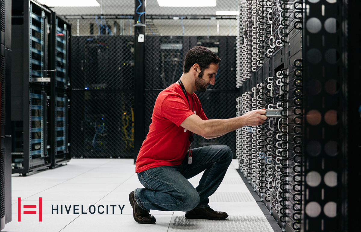 Man kneeling in front of server cabinet with Hivelocity logo by his foot