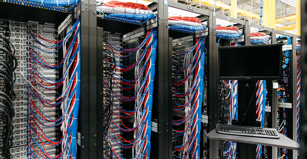 Back end of a row of server cabinets, with multicolored bundles of wires running along their tops