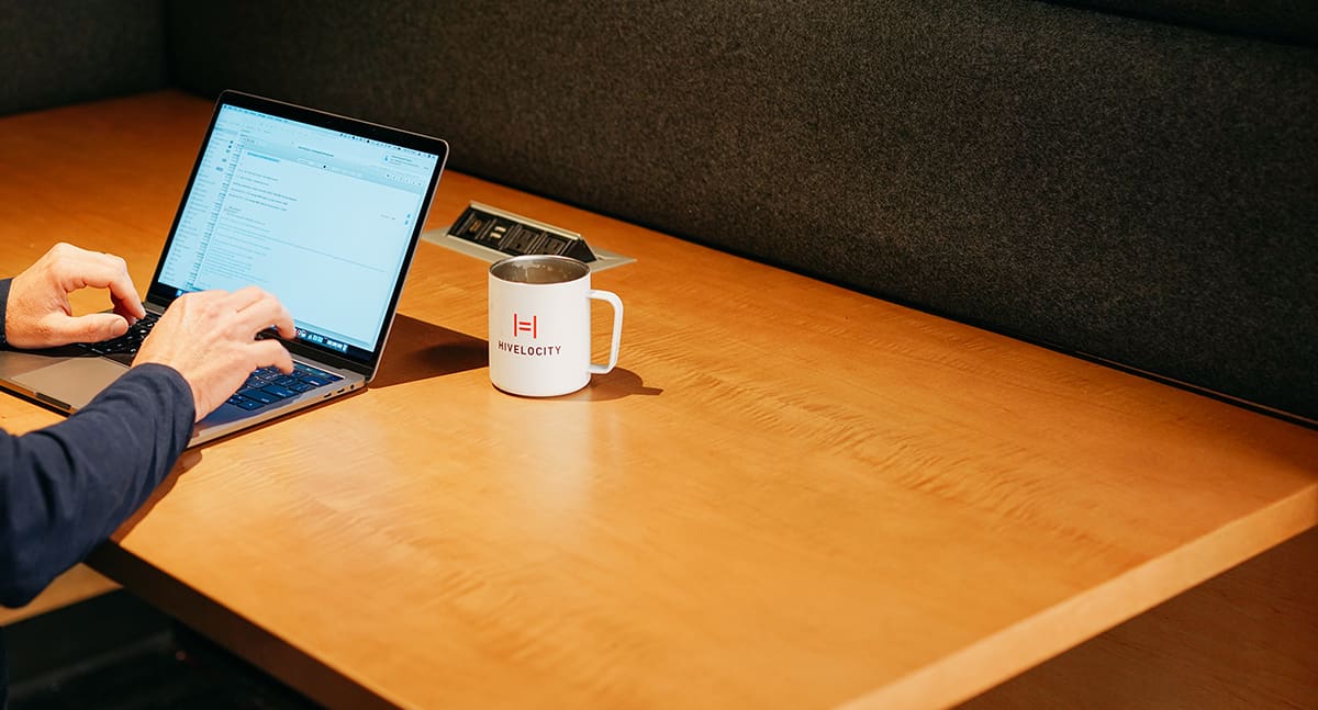 Hivelocity mug on a desk next to someone typing on their laptop